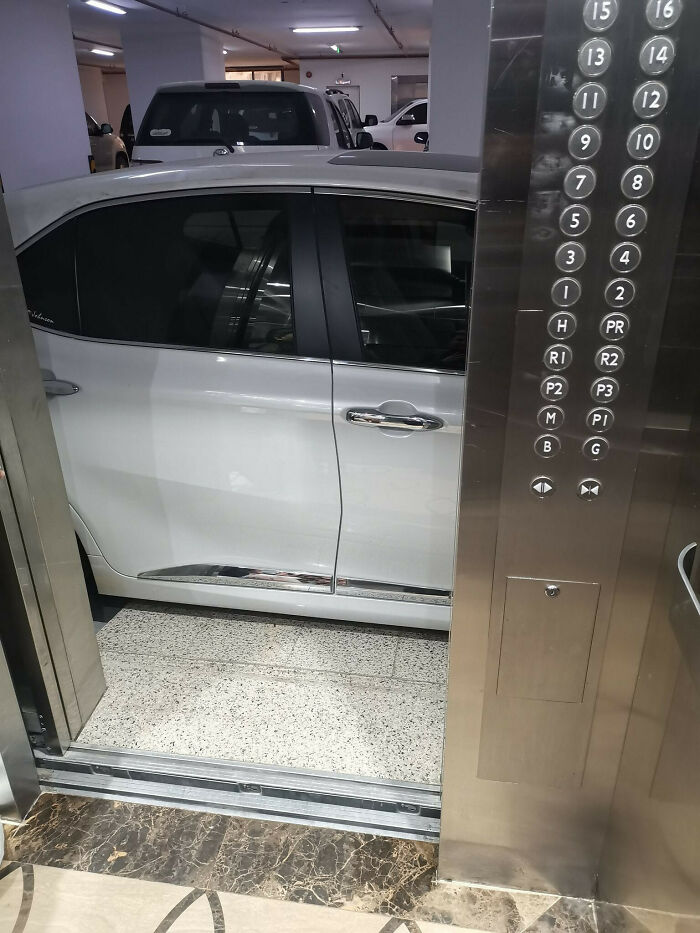 A white car parked halfway into an elevator, showing poor parking common sense by a neighbor.