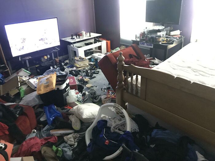 A messy male living space filled with clothes, shoes, and miscellaneous objects, with a TV on one side.