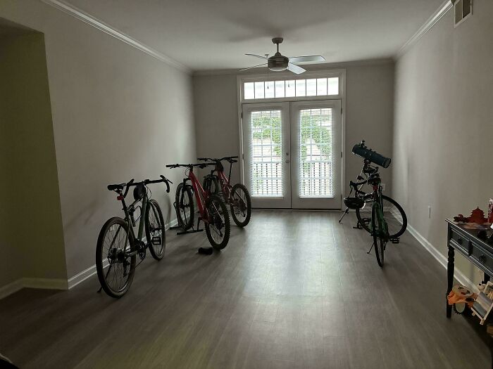 A minimalist male living space with four bikes and a telescope near a set of french doors.