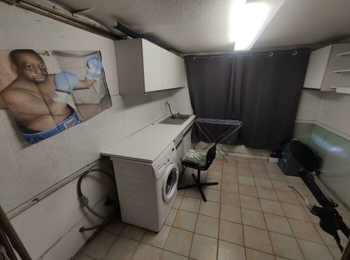 A spartan male living space with a washing machine, utility sink, and a boxing poster, showing a unique living style.
