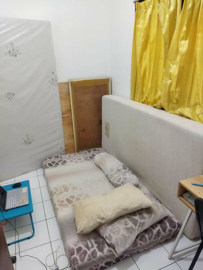A minimalist male living space with a mattress on the floor, pillows, and bright yellow curtains, inspiring how to live.