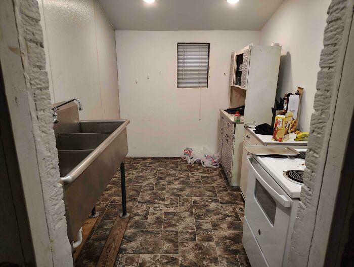 A messy kitchen in a male living space with a large sink, stove, and dirty floors, depicting how not to live.