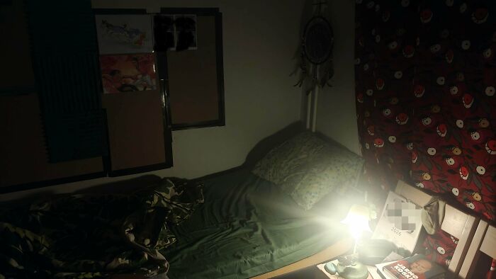 A dim male living space featuring a bed, a small lamp, and wall decor.