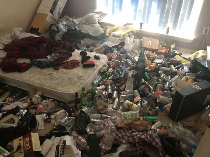 An extremely messy male living space with a mattress on the floor surrounded by trash and empty cans.