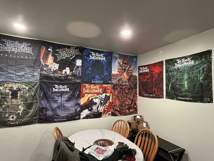 A male living space decorated with multiple band flags hanging on the wall above a dining table.