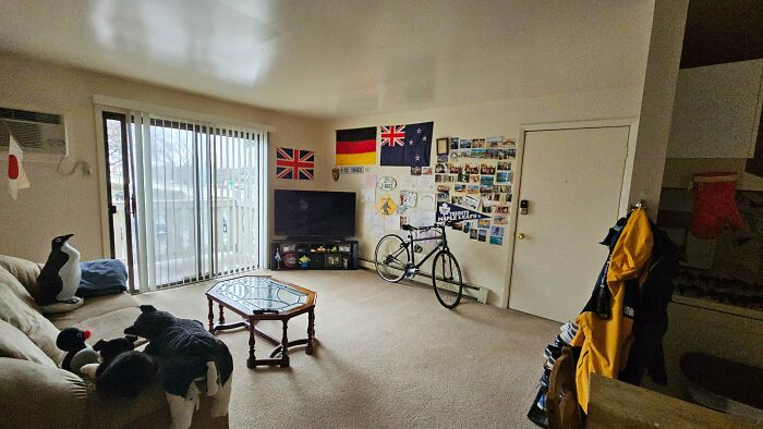 A cluttered male living space with flags, a TV, a bicycle, and a couch, offering inspiration for living.