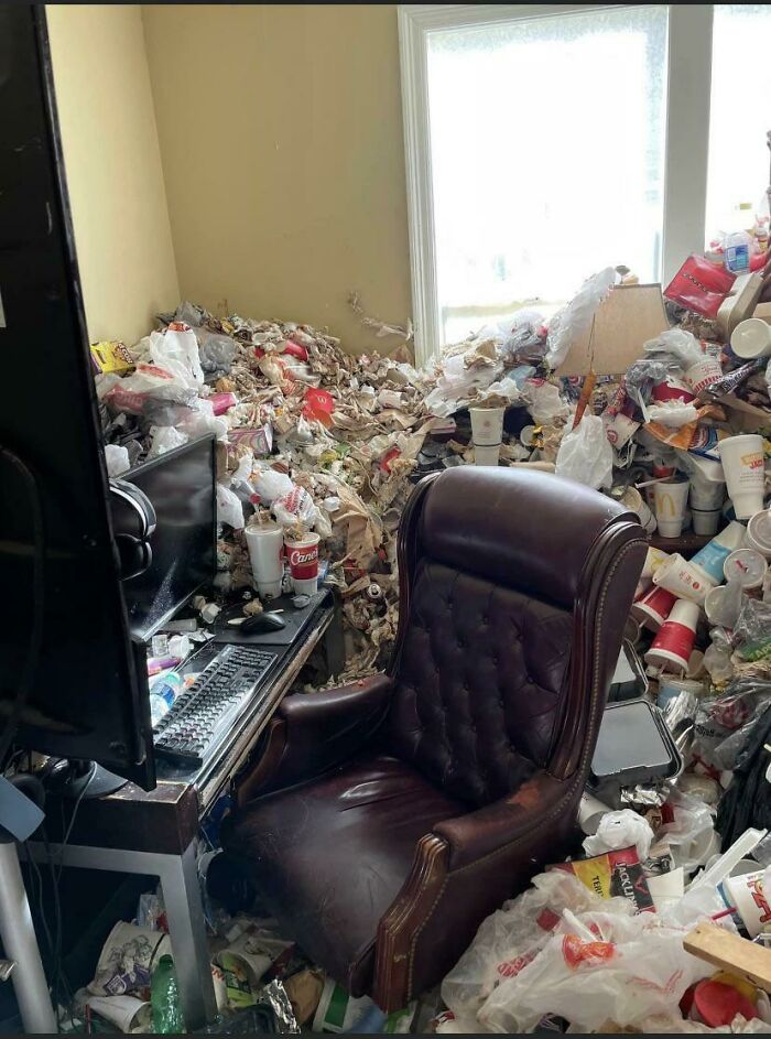 An office chair surrounded by an immense amount of fast-food containers and garbage, illustrating male living spaces gone wrong.