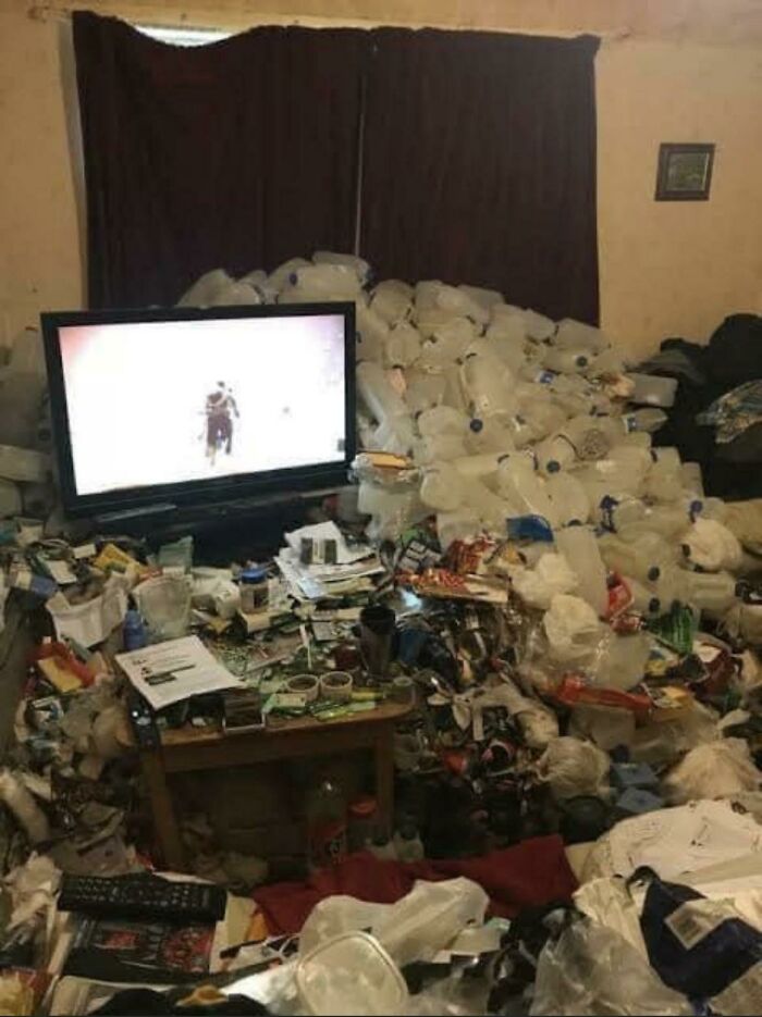 A room overflowing with empty water bottles and trash around a television, demonstrating unkempt male living spaces.