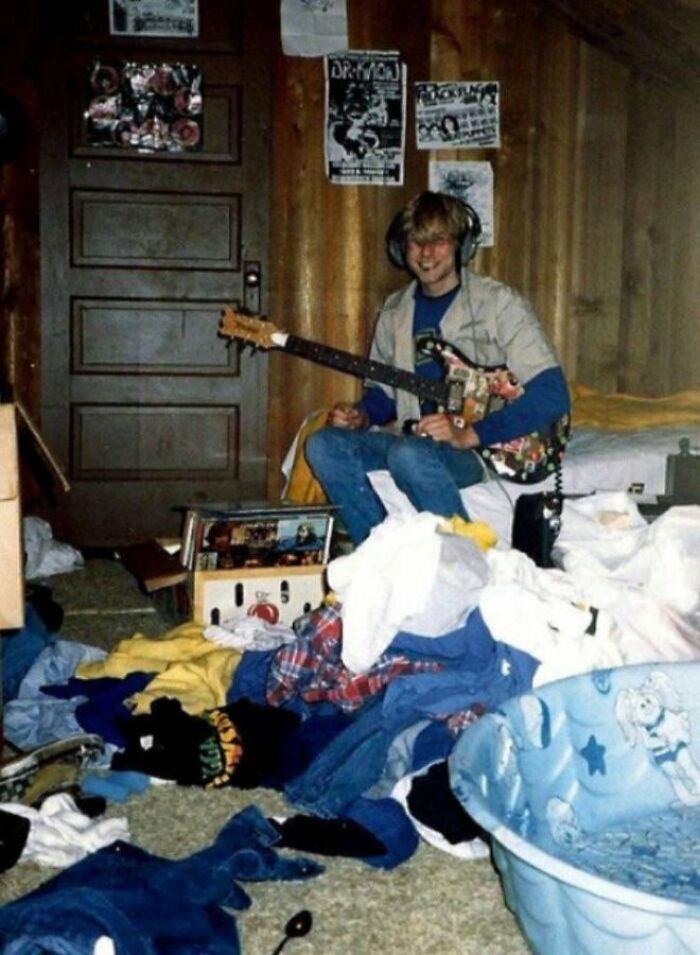 A young male playing guitar in a messy room, showcasing male living spaces inspiration.