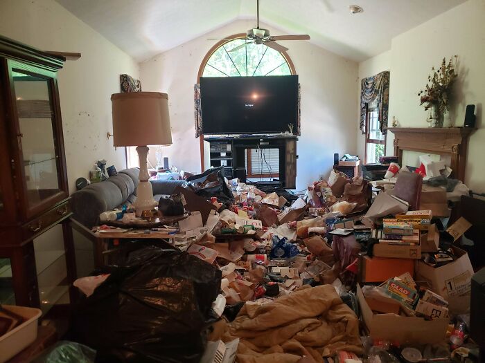 An extremely cluttered male living space with trash, boxes, and miscellaneous items strewn across the floor.