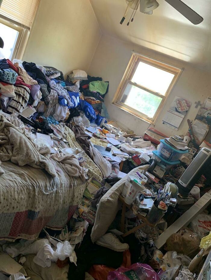 An extremely messy male living space, filled with clothes, trash, and various items piled high.
