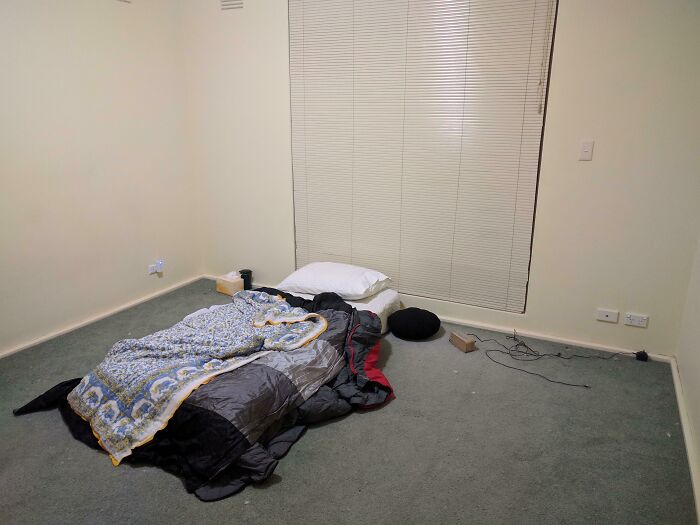 A sparsely furnished room with a sleeping bag on the floor, portraying a minimalist but uninviting male living space.