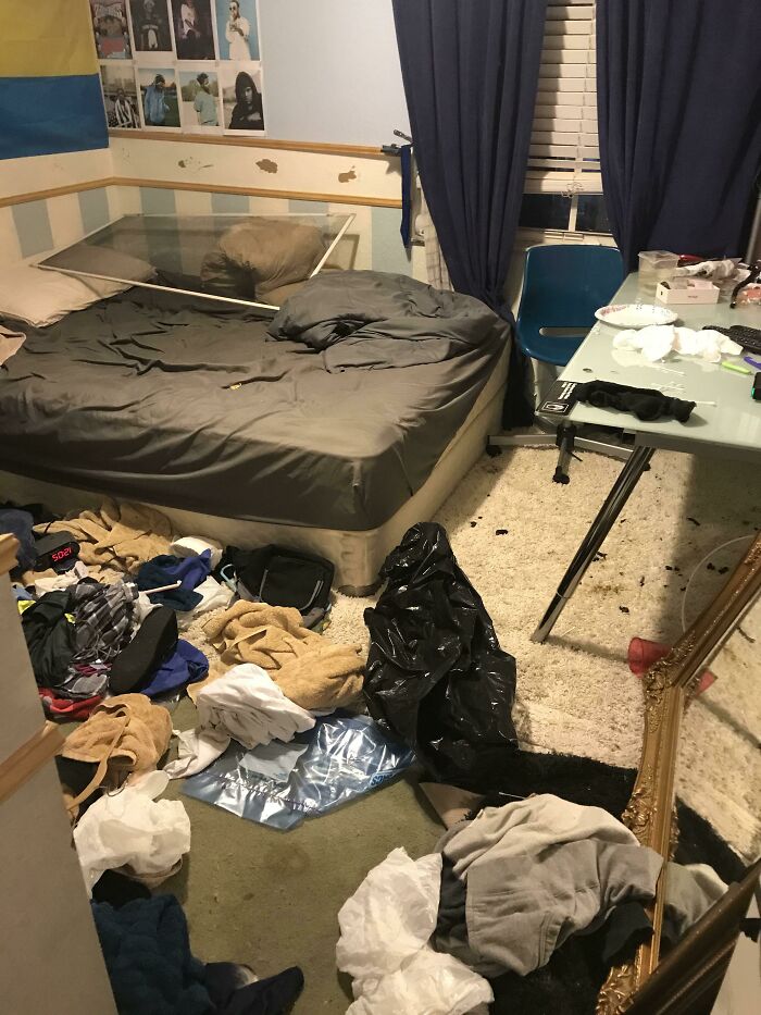 A messy bedroom with clothes, trash, and an unmade bed, showing an example of how not to live in male living spaces.