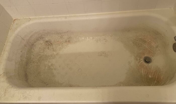 A dirty bathtub filled with hair and grime, illustrating how not to live in male living spaces.