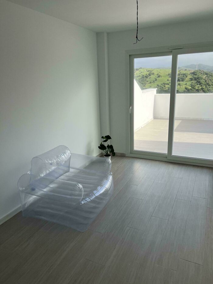 A minimalistic male living space featuring an inflatable chair and a potted plant, with a balcony view of green hills.