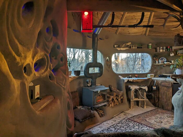 A cozy, rustic male living space with a wood-burning stove, unique sculpted walls, and natural light.