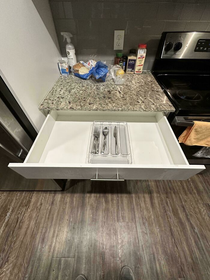 A minimalist kitchen with an open drawer showing a cutlery organizer, reflecting a male living space.