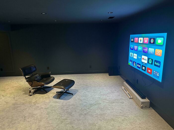 A minimalist home theater with a black armchair and ottoman, large projected screen showing apps, a great male living space.