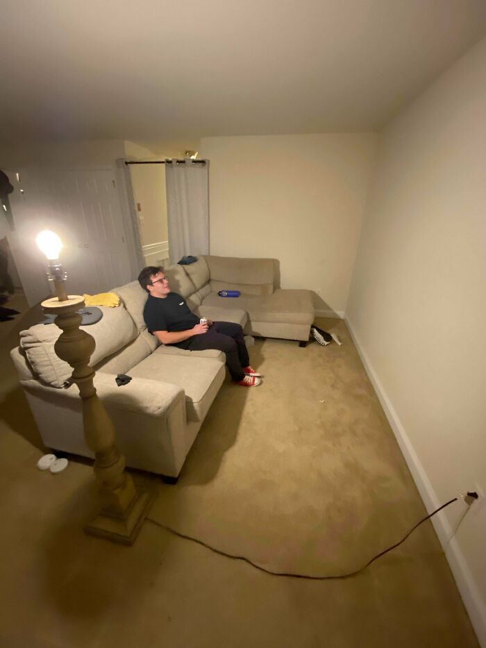 A man relaxing on a beige sectional sofa in a dimly lit living space, a prime example of male living spaces.