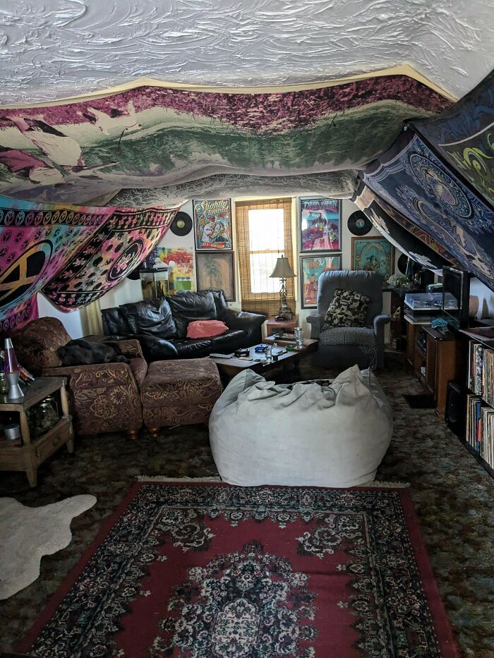 An eclectic male living space with tapestries on the ceiling, a leather sofa, and a large white bean bag chair.
