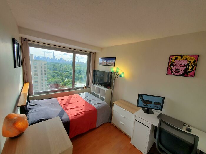 A male living space with a bed, desk, city view, and pop art, offering living inspiration.