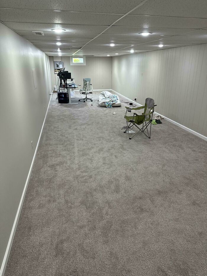 A spacious, carpeted male living space with a desk, office chairs, and a green camping chair.