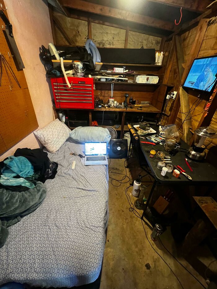 A cramped male living space with a bed, a cluttered workbench, and a TV, illustrating how not to live.
