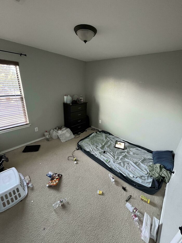 A messy, unkempt male living space with an air mattress on the floor and scattered trash, showing how not to live.