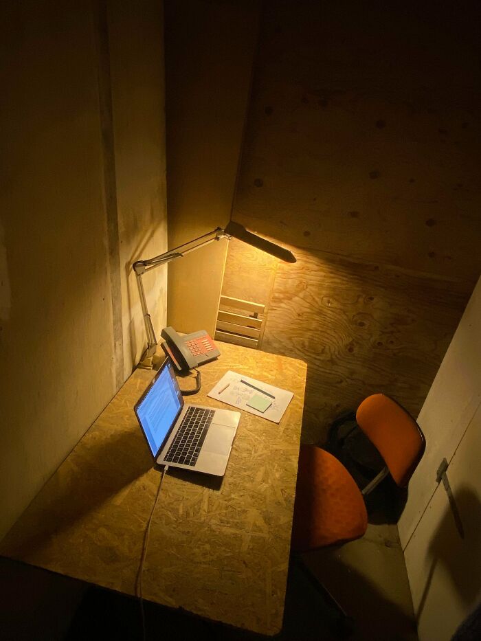 A small, dimly lit male living space with a laptop and lamp on a wooden desk, showcasing how not to live.