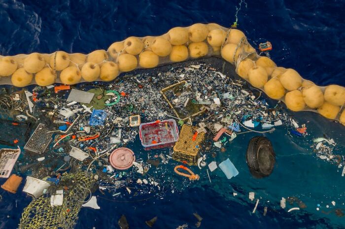 An aerial view of a large net in the ocean, filled with a massive collection of trash and debris, illustrating the global trash problem.