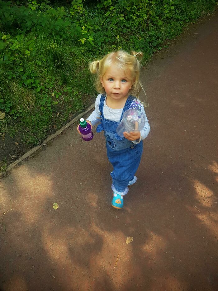 A young child walking on a path, holding a bottle and looking at the camera. She is a real influencer for good.