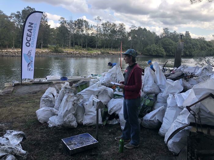 Influencers clean trash from a riverbank, highlighting the global trash problem and the importance of environmental action.