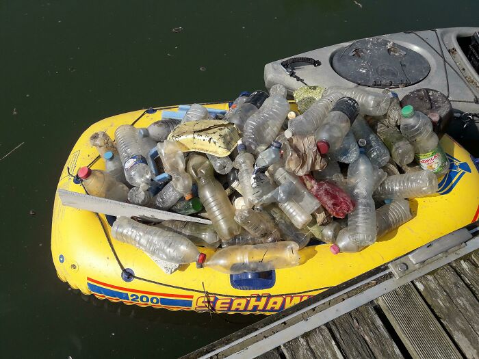An inflatable yellow boat filled with plastic bottles and other trash, showing the problem of trash taking over the world.