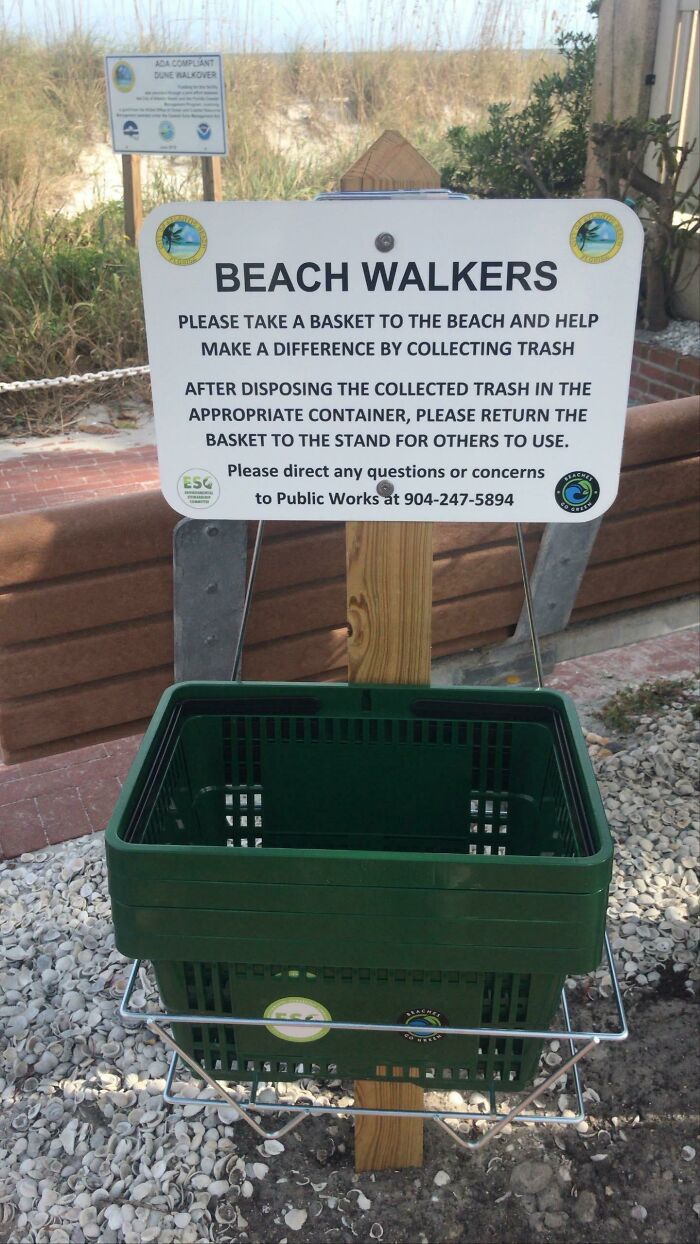 A sign for beach walkers to collect trash, with a green basket below it, promoting efforts to combat trash.