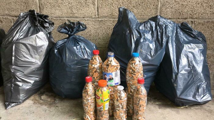 Several plastic bottles filled with cigarette butts and large trash bags, highlighting the trash taking over the world.