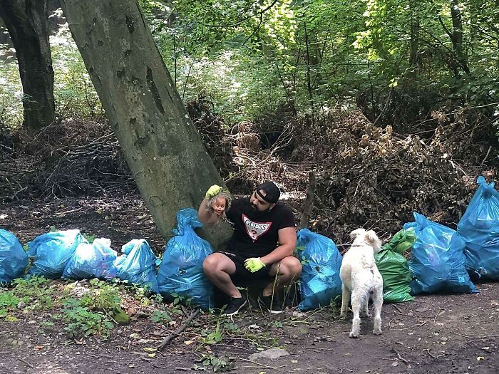 A man with a dog, surrounded by blue trash bags in a forest, showing efforts to clean up trash taking over the world.