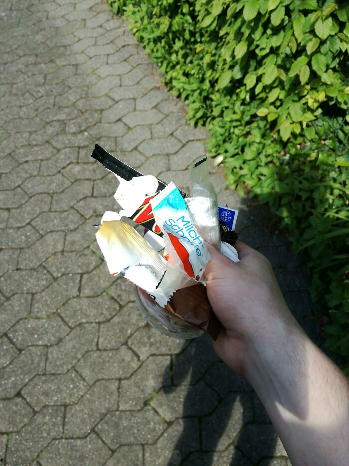 A hand holding a small collection of candy wrappers, representing the everyday trash that takes over the world.