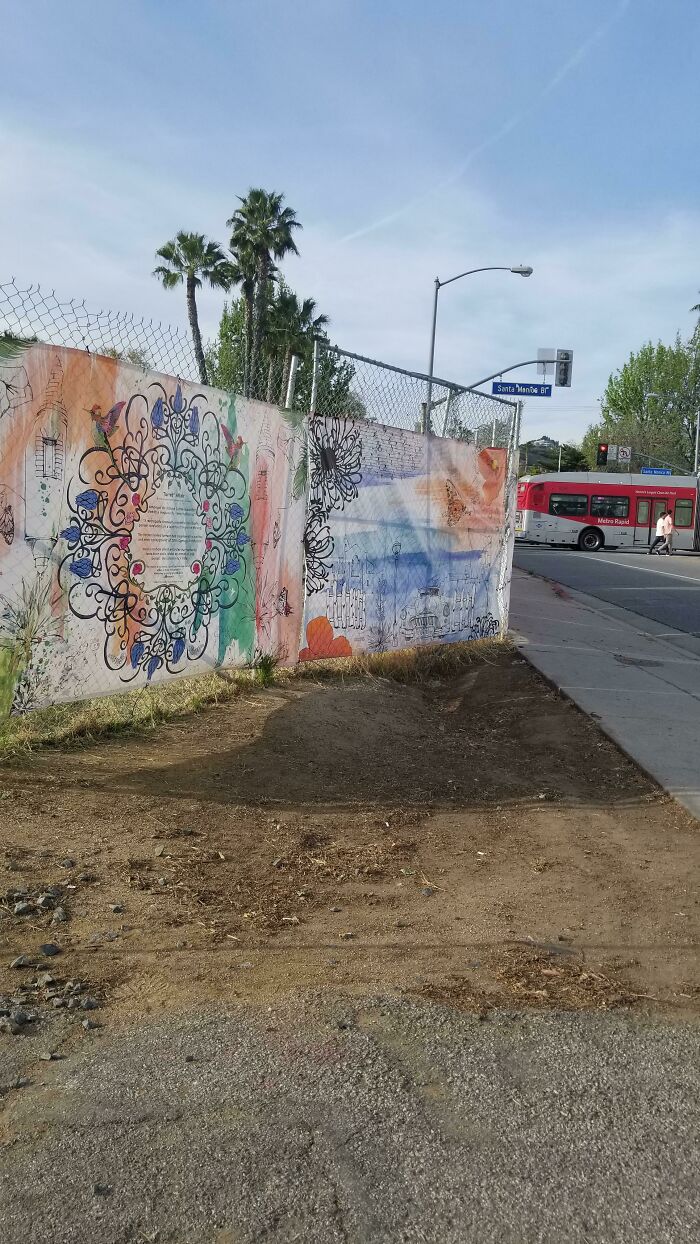 An artistic street mural on a fence, overlooking a street with a bus, promoting a clean environment without trash.