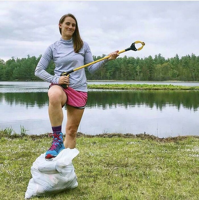 A woman stands triumphantly on a bag of collected trash, influencing others to clean up the world.