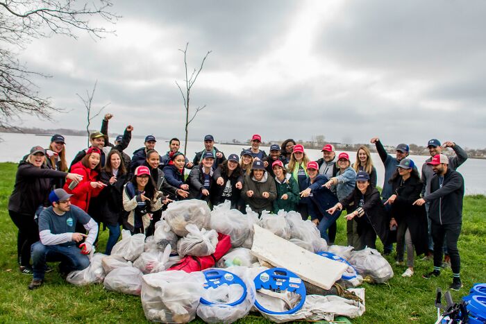 A group of people, dressed in casual clothes and hats, pose proudly in front of large bags of trash they collected.