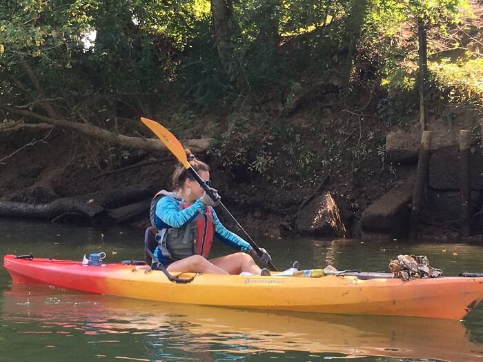 A woman paddles a kayak, collecting trash from the river to become a positive influencer.