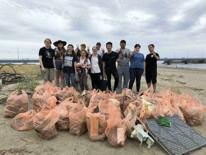 Influencers clean up trash from the world, posing with bags of collected garbage on a beach.