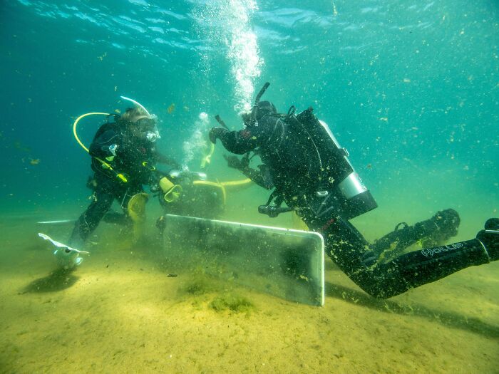 Two divers underwater, appearing to collect trash from the seabed, showcasing people's efforts against trash.