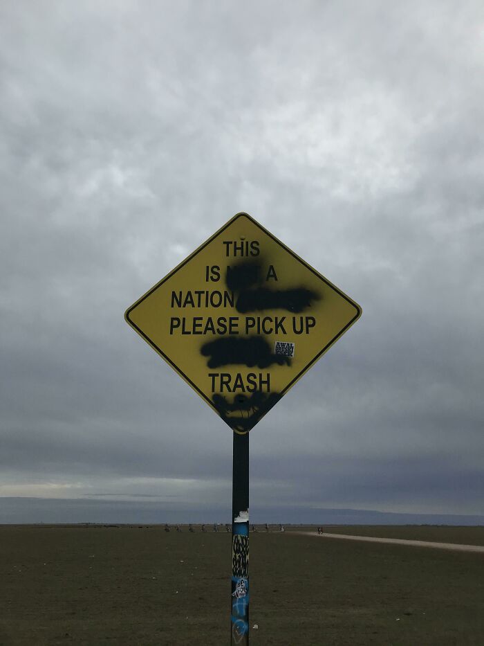 A yellow diamond-shaped sign that reads This is a nation, please pick up trash, urging people to manage trash.