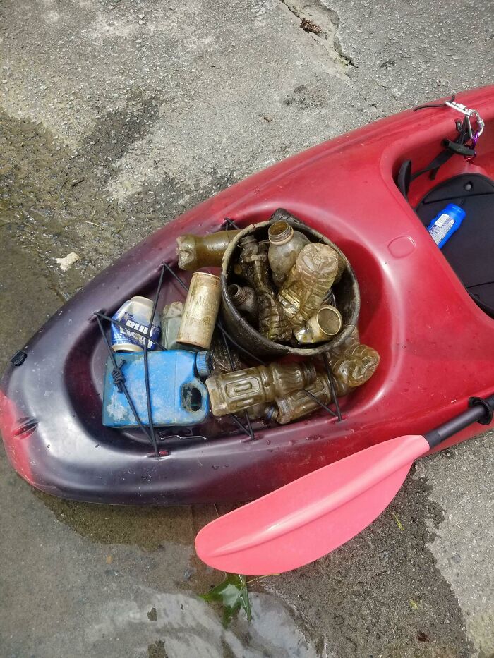 A red kayak filled with trash, including plastic bottles and cans. People are taking over the world.