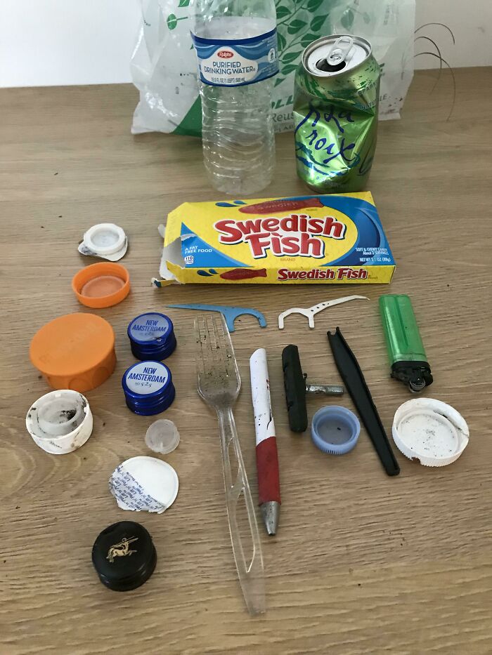A collection of trash on a wooden surface, including plastic bottles, a can, and various plastic items. People are taking over the world.