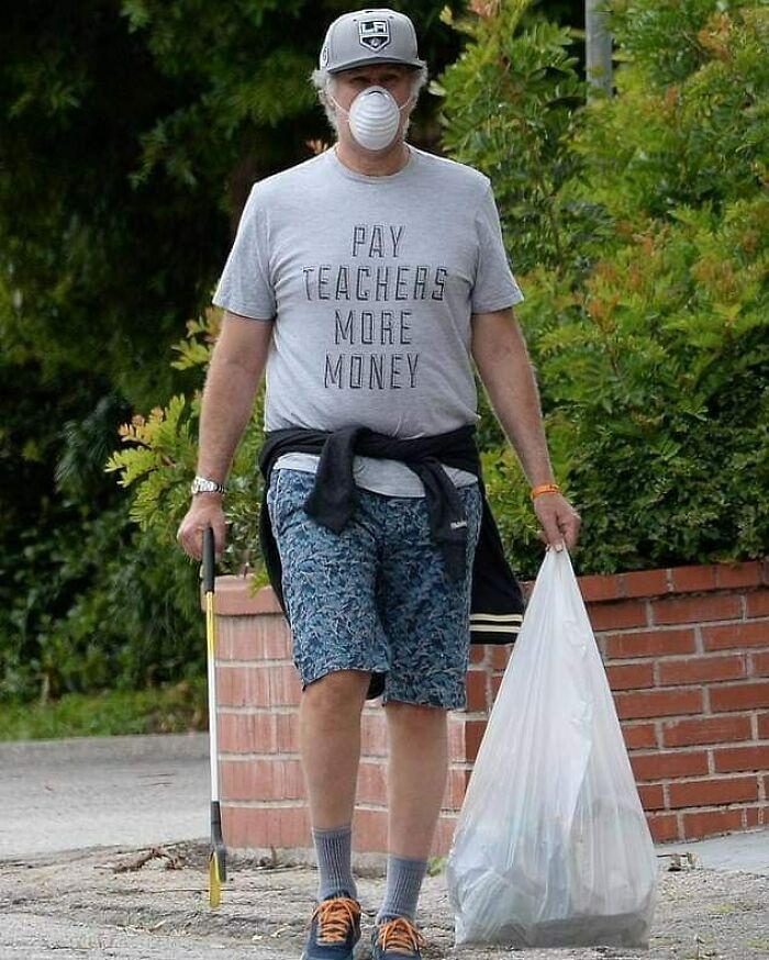Man wearing a mask and a 'Pay Teachers More Money' shirt, holding a trash grabber and a bag of collected trash.