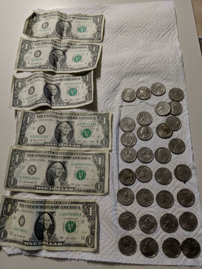 Six one-dollar bills and numerous coins laid out on a paper towel, representing money found while cleaning up trash.