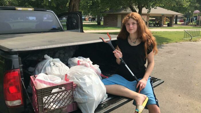 A young person sits on a truck bed filled with bags of trash, holding a trash picker, being an influencer against trash.