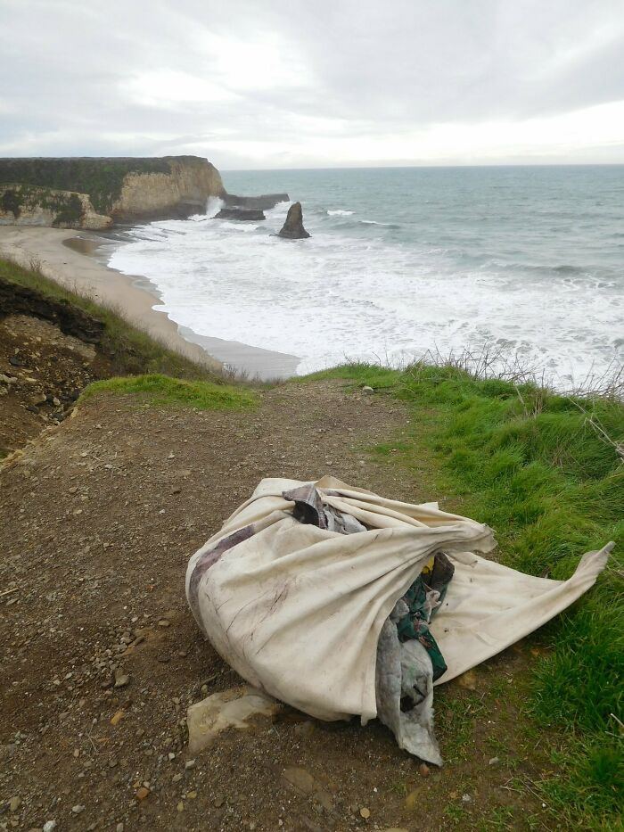 A large bag of trash sits on a cliff overlooking a beach, showing how trash takes over the world.